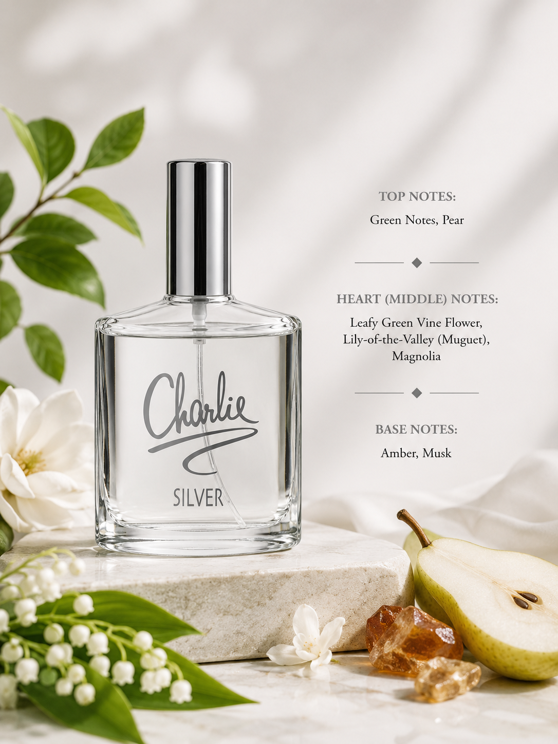A clear rectangular perfume bottle labeled 'Charlie SILVER' with a silver cap, styled on a stone slab with green leaves, white flowers, a pear, and amber crystals. Text on the right lists the scent notes: top notes green, pear, and pear; heart notes lady green vine flower, lily of the valley, magnolia; base notes amber, musk.