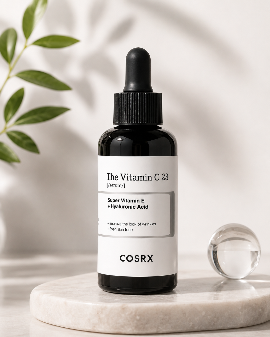 COSRX The Vitamin C 23 Serum displayed on a light stone pedestal with fresh greenery and a glass accent, illuminated by soft natural light for a clean, premium skincare aesthetic.